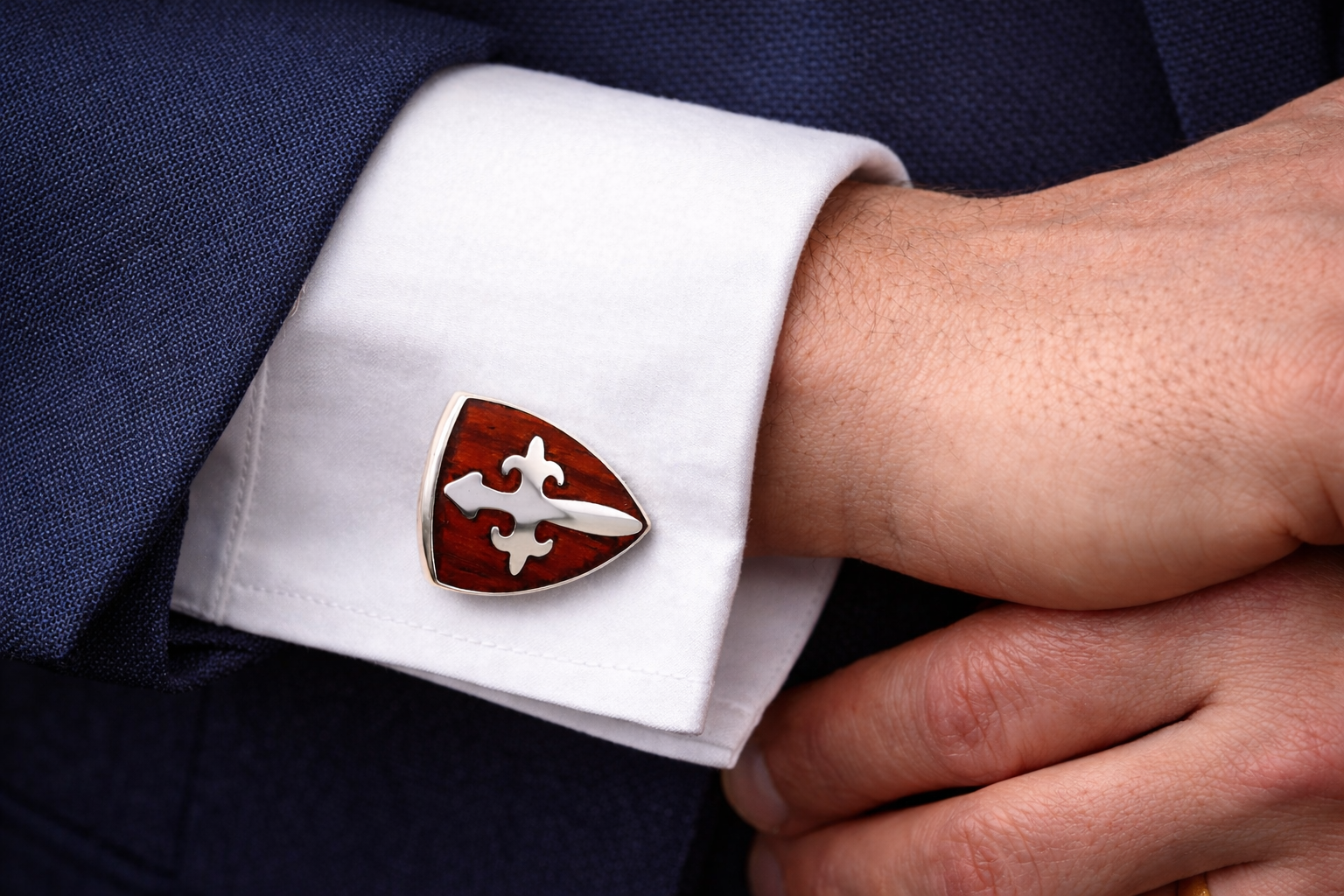 Close-up of a cufflink with a Christian religious cufflinks stainless steel and natural wood worn on a cuff, against a dark suit background.