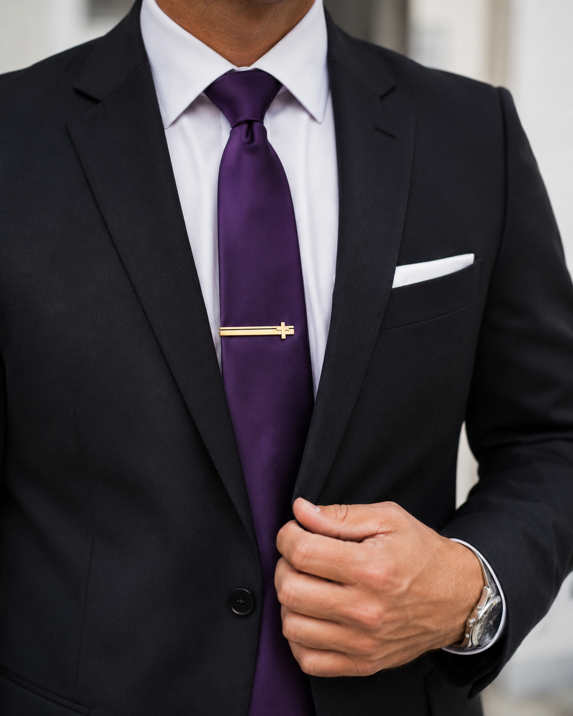 Man wearing a black suit with a purple tie and white pocket square. Cross Tie Clip