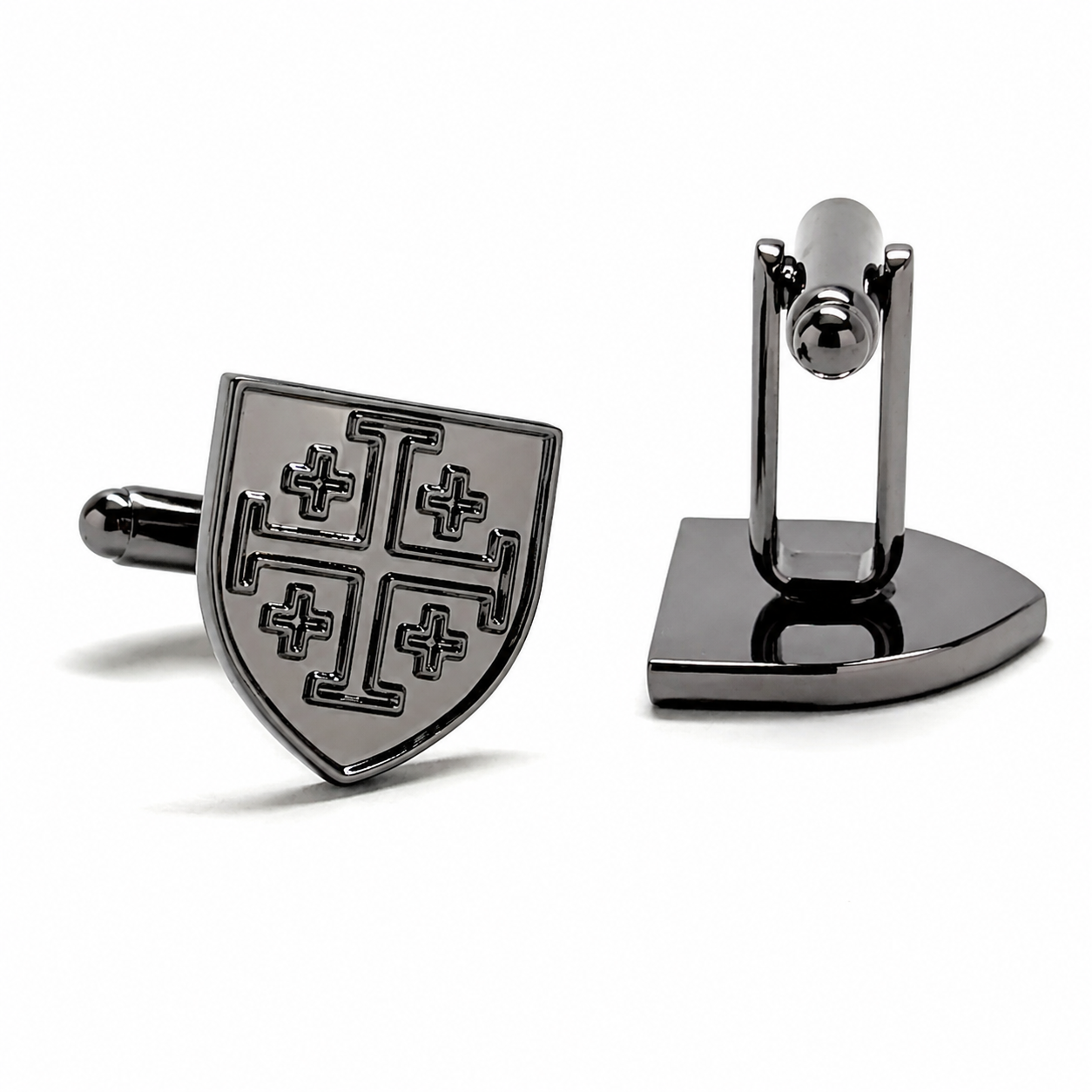 A pair of dark metallic cufflinks on a clean white background. One cufflink is shown from the front, featuring a shield-shaped face with a blackened cross motif on a silver-toned base.