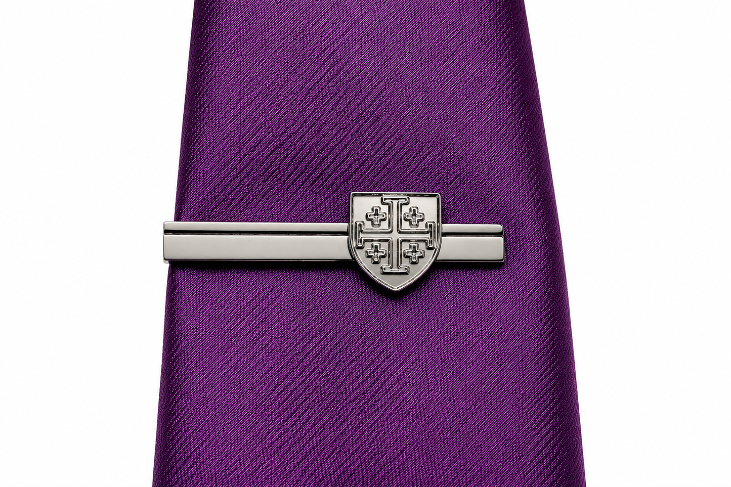 A silver-toned metal tie bar with a shield crest design, shown clamped onto a textured purple necktie against a plain white background.