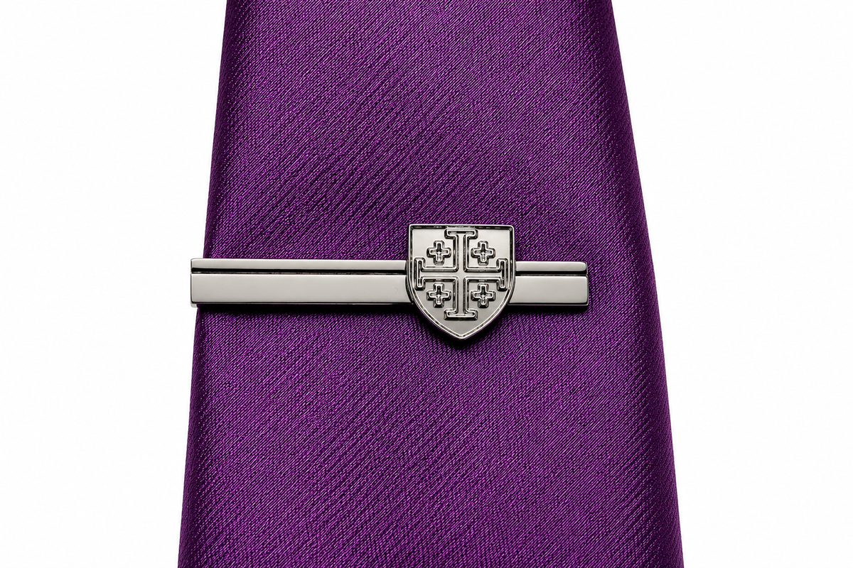 A silver-toned metal tie bar with a shield crest design, shown clamped onto a textured purple necktie against a plain white background.