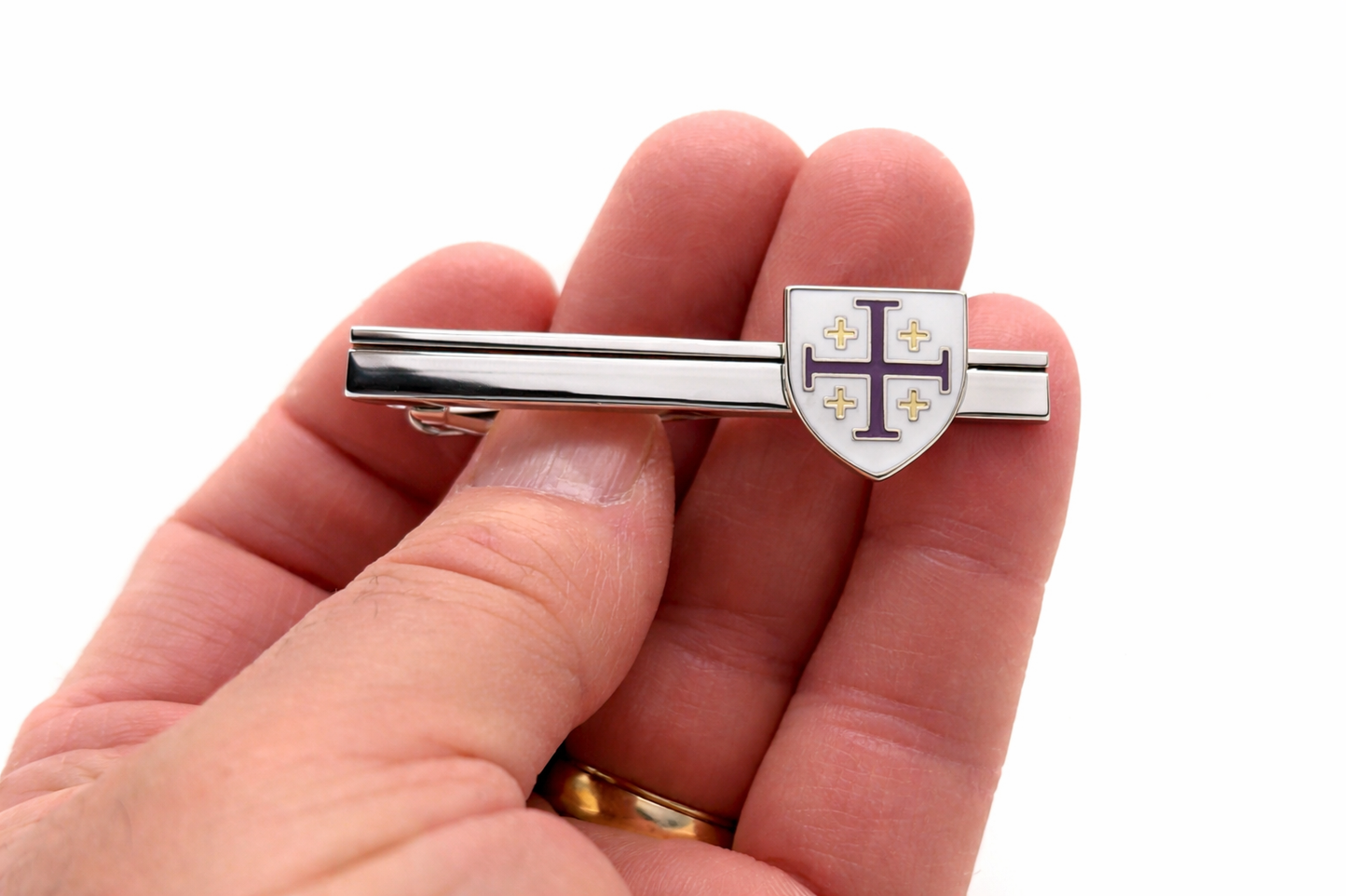 Silver tie clip with a shield design held between fingers on a white background