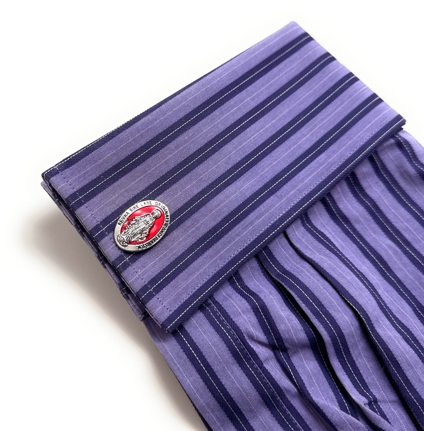 Folded purple striped shirt with a cufflink on a white background
