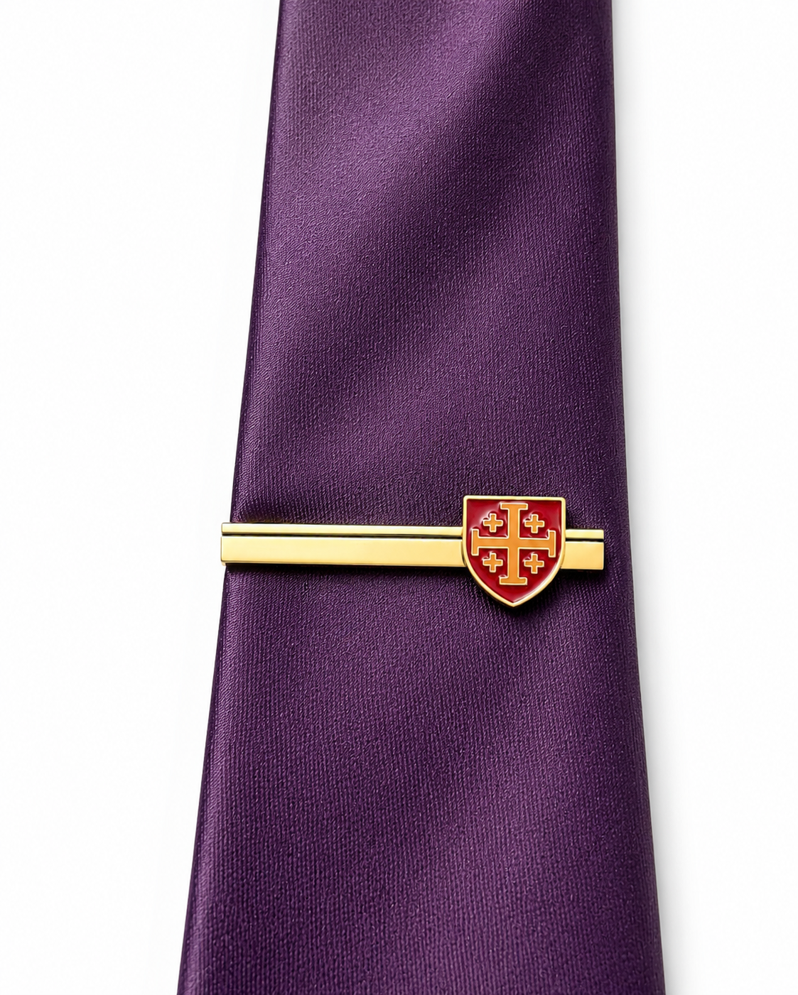 A purple silk tie secured with a gold-tone tie bar featuring a red and gold shield crest, set against a plain white background.