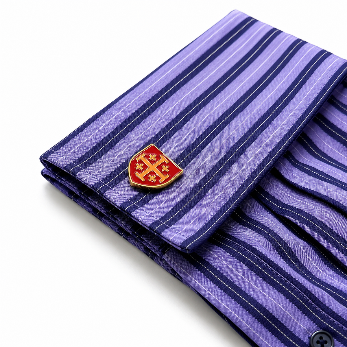 A folded purple striped dress shirt with a red and gold shield-shaped cufflink pin, shown on a clean white background.