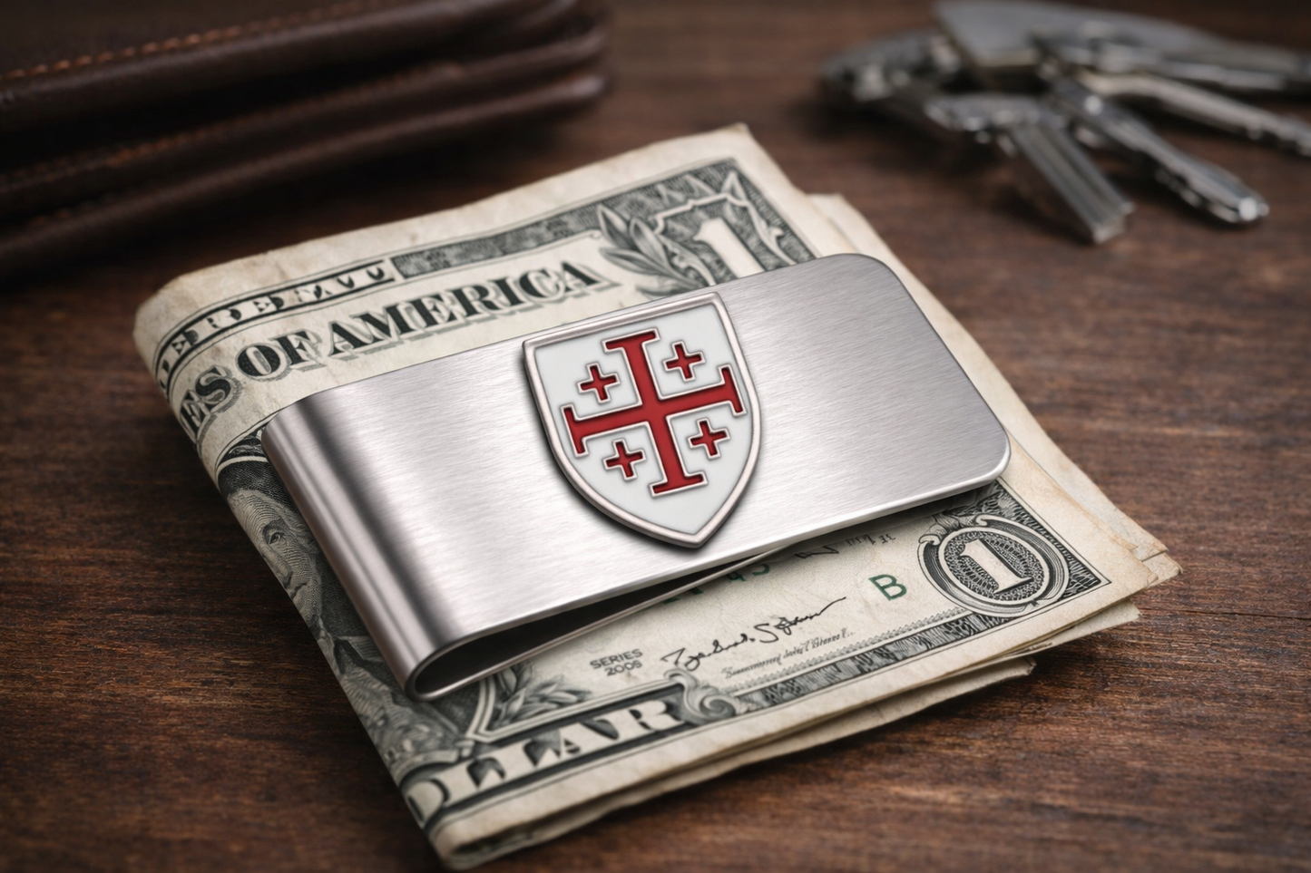 Silver money clip with a shield design Jerusalem Cross stainless steel money clip Christian religious accessory for men on top of U.S. dollar bills on a wooden surface.