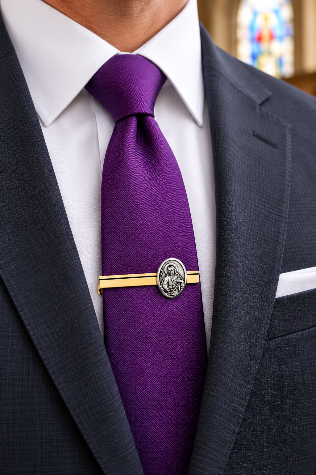 A close-up of a purple silk tie with a gold tie bar featuring a silver-toned medallion, worn with a white dress shirt and dark gray suit jacket.