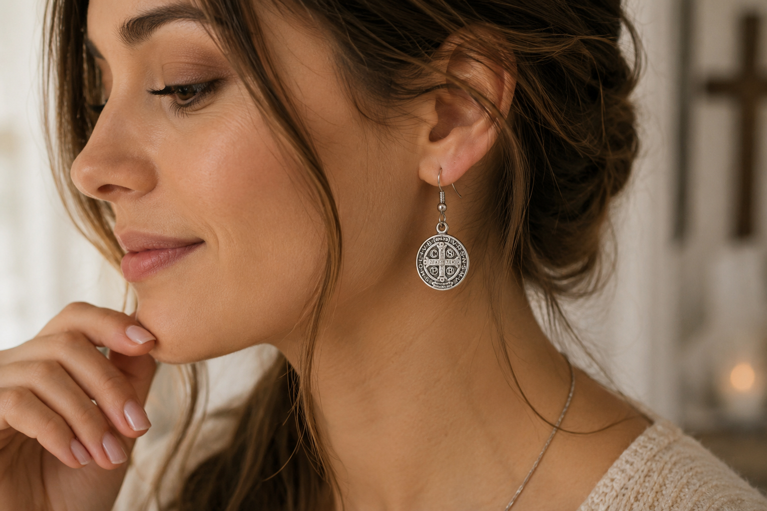Close-up of a woman wearing silver earrings with a blurred background. Saint Benedict Medal Earrings Silver Catholic Christian Dangle Earrings for Women