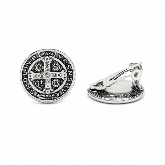 Silver Saint Benedict clip-on earrings with detailed Catholic medal design on a pure white background.