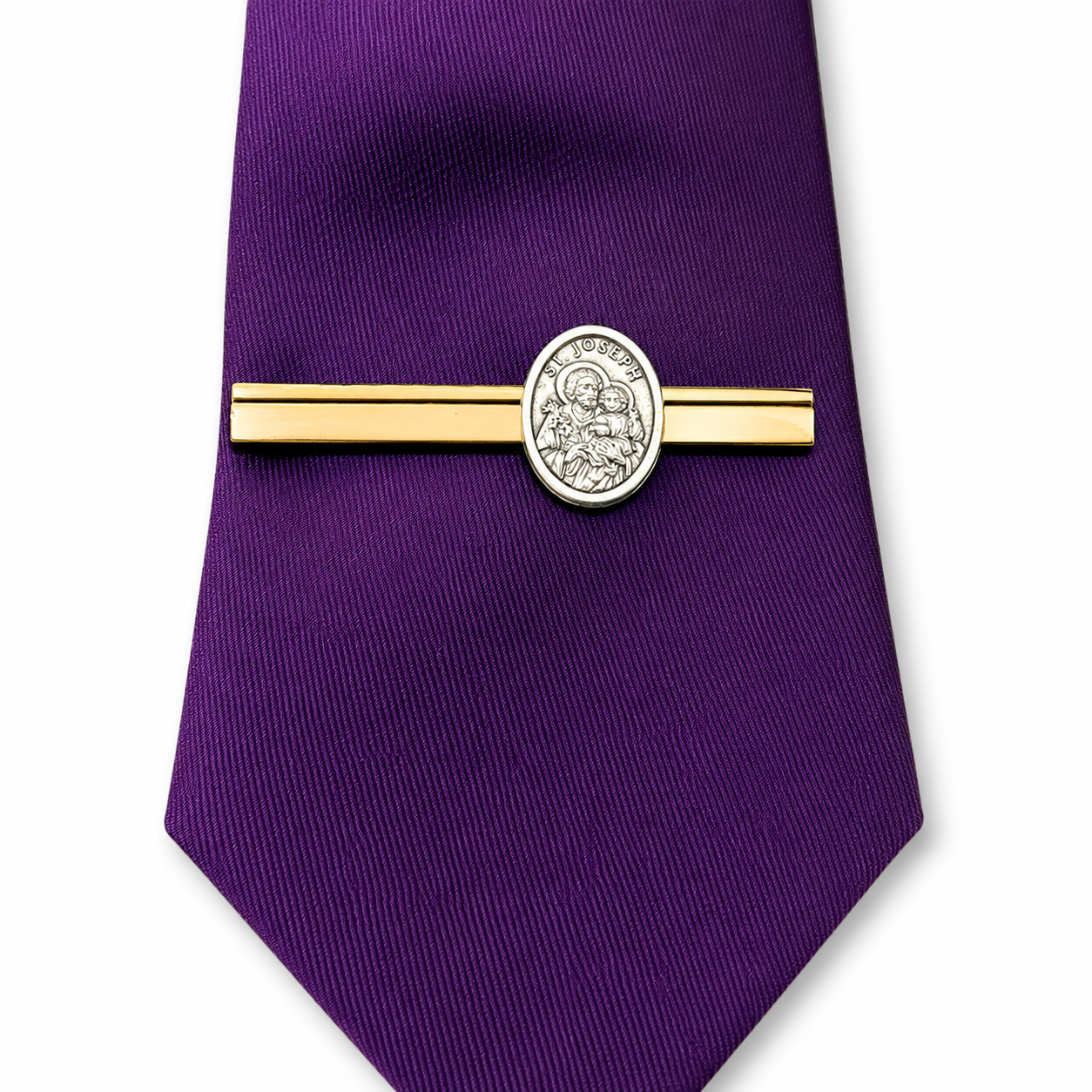 A purple silk necktie with a gold and silver tie clip featuring an oval Saint Joseph medallion, set against a plain white background.