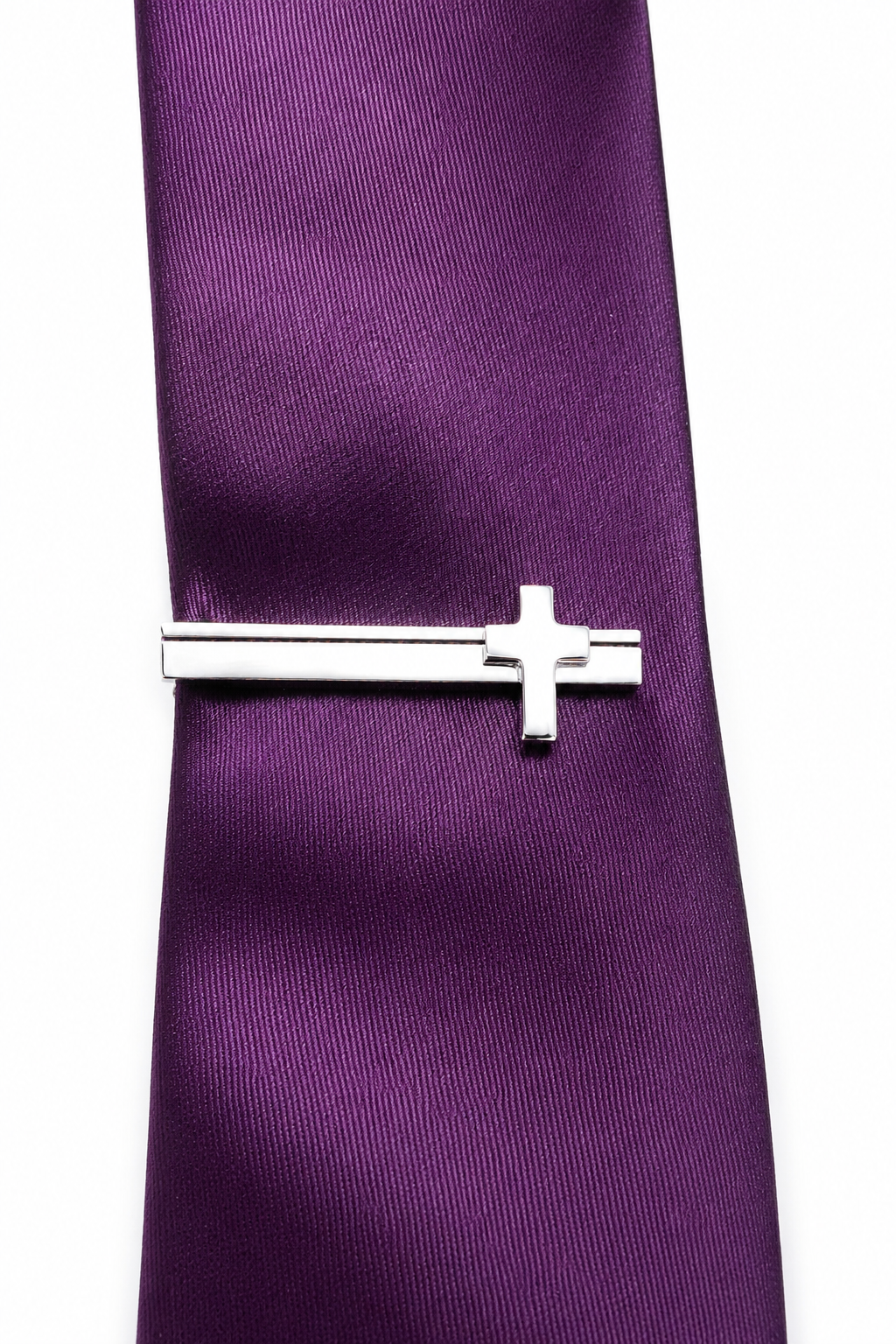 Silver cross tie clip on a purple tie against a white background