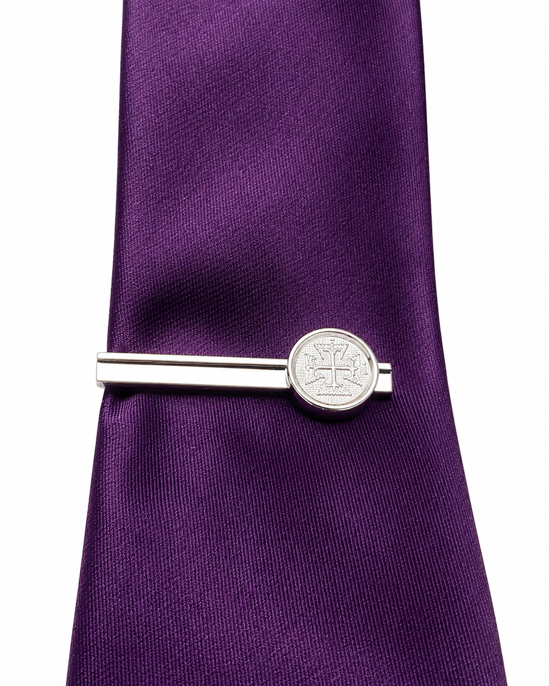 Silver cross tie clip on a purple tie against a white background
