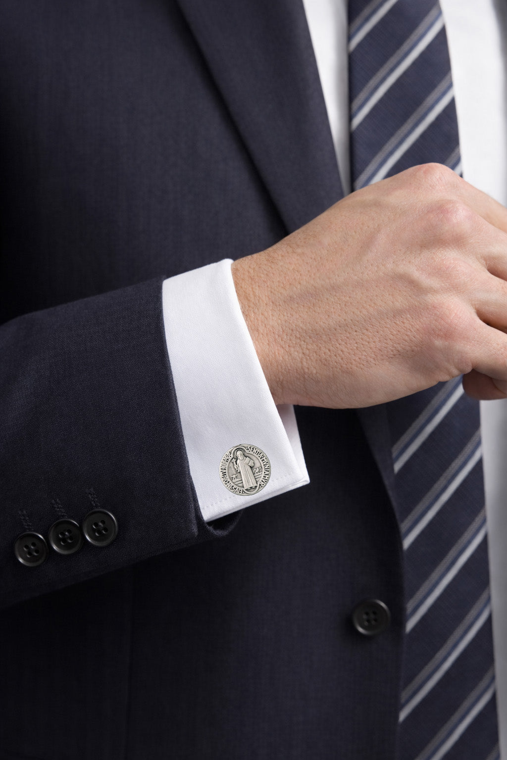 Close-up of a person wearing a dark suit with white cufflinks and a striped tie.