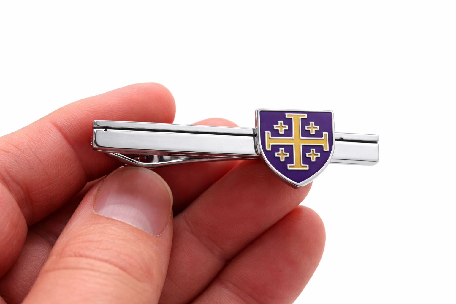 Tie clip with a purple and gold emblem held in a hand against a white background