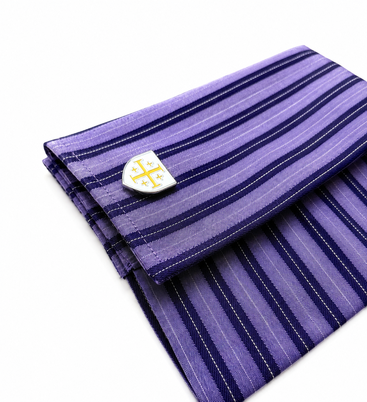 Purple striped silk pocket square with a white shield-shaped cufflink featuring a gold cross, displayed on a clean white background.
